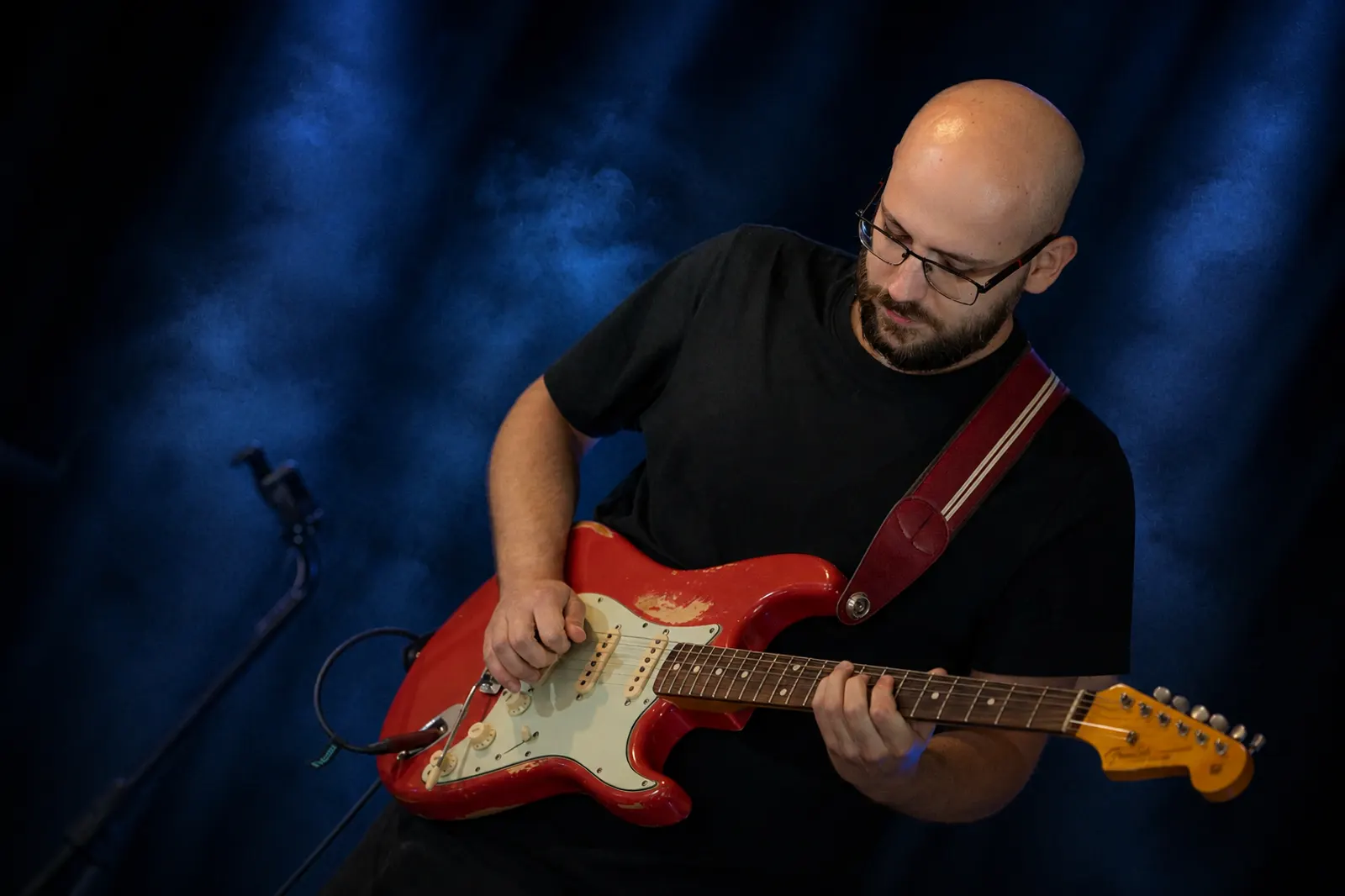 Guitar player performing on stage with a red electric guitar under blue spotlight