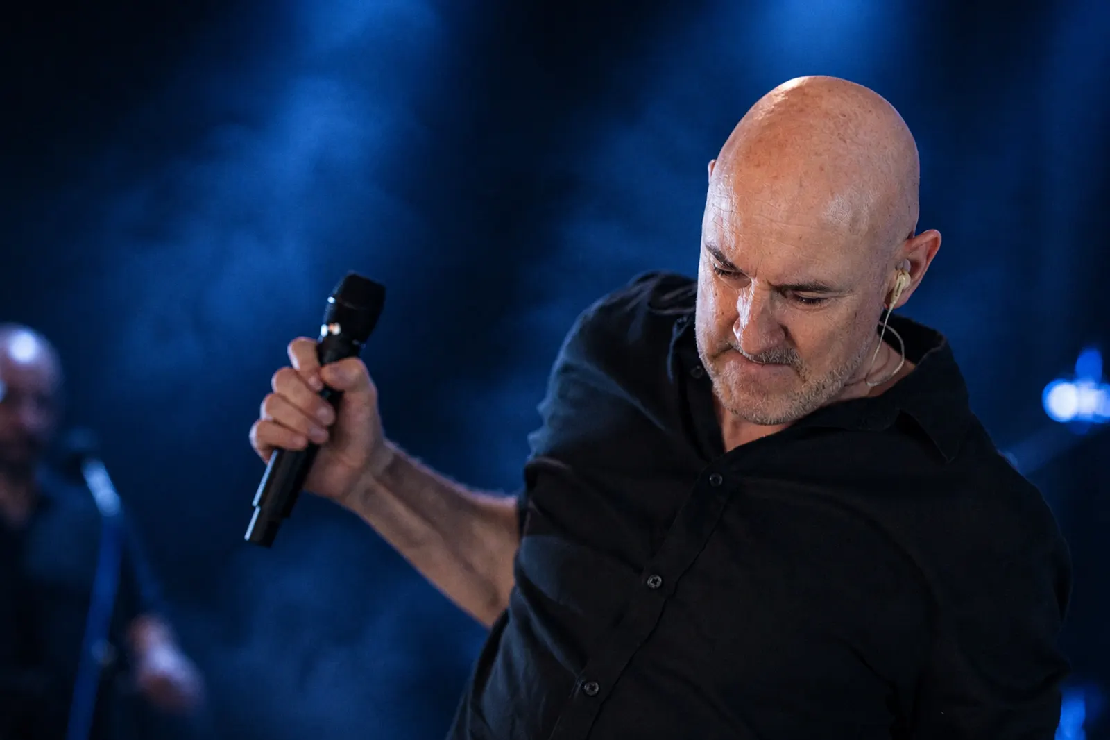 Vocalist Robert Fàbrega Ferrer performing on stage with a microphone under blue spotlight
