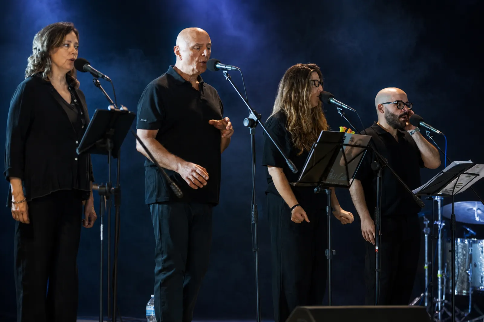 Four vocalists singing on stage with microphones under blue stage lighting