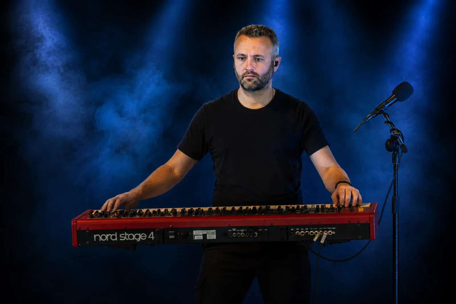 Keyboard player performing on stage with a Nord Stage keyboard under blue spotlight